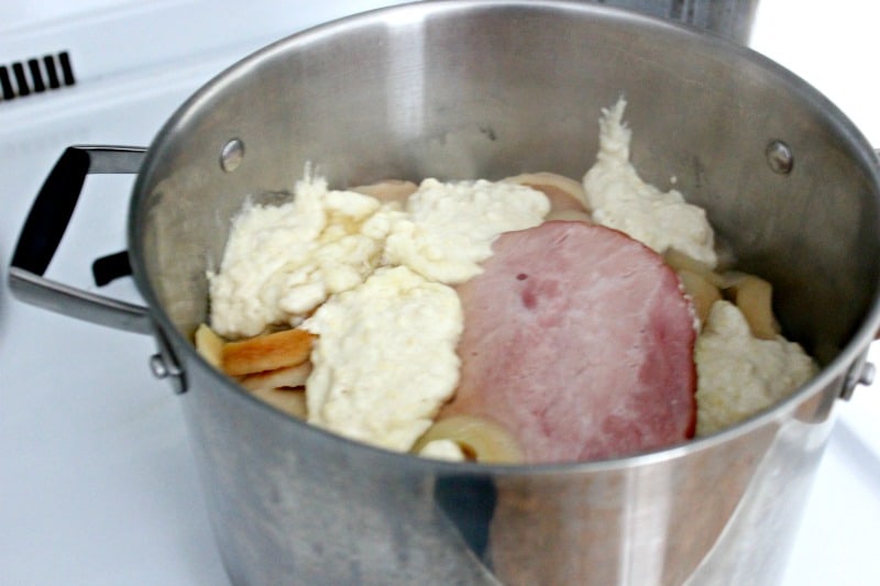a silver pot with ham, apple rings, and dumplings cooking
