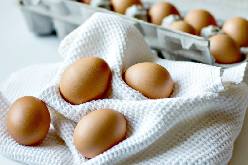 fresh eggs on a white towel in front of an egg carton