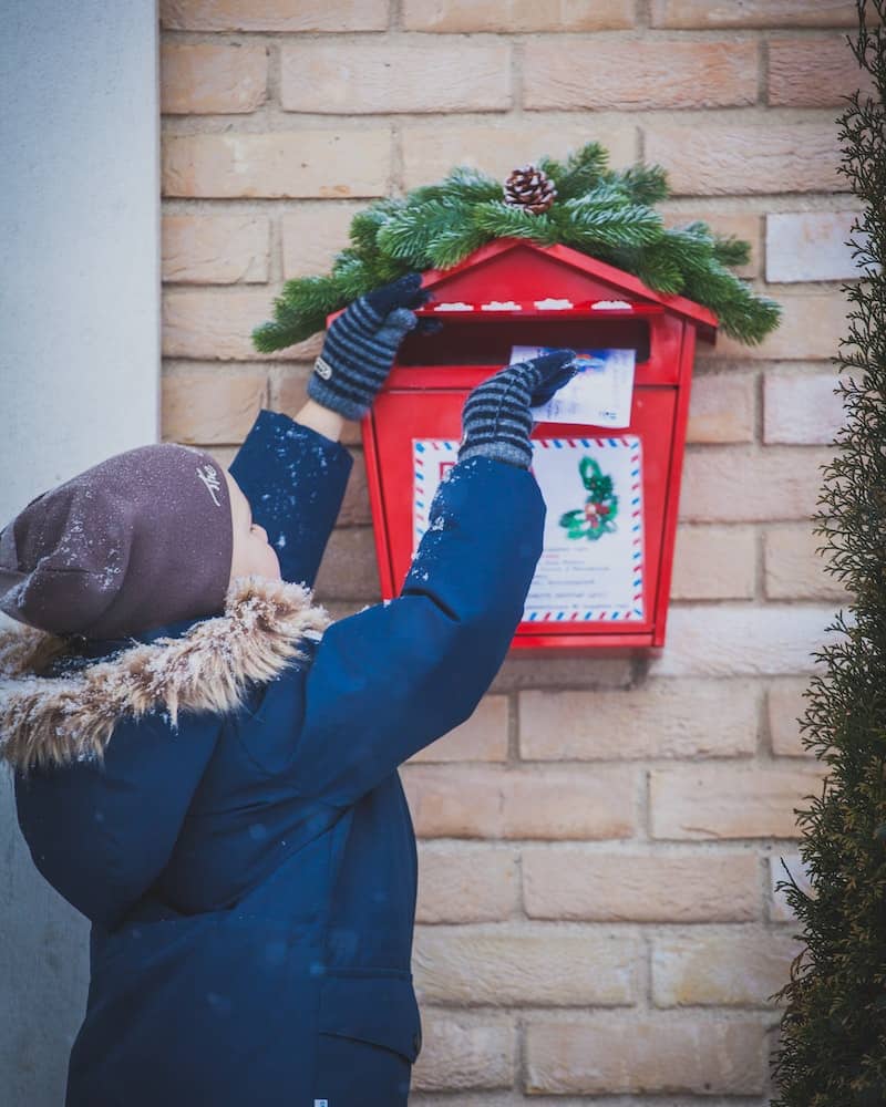a child putting a letter in a Christmas decorated mailbox