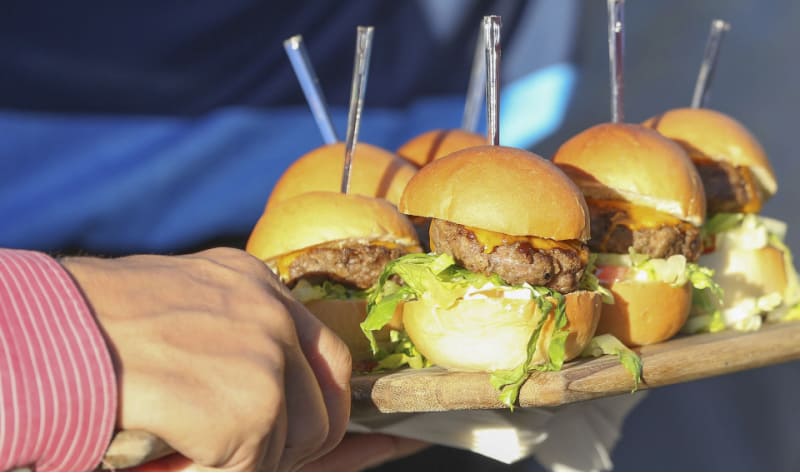 a woman carrying a platter of sliders from a build your own slider bar