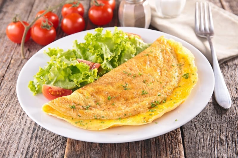 an omelette with salad on a white plate near tomatoes