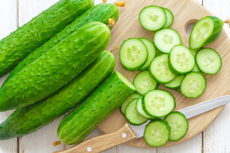 cucumbers being sliced on a brown cutting board