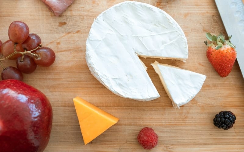a wedge of brie and fruit on a wooden cutting board