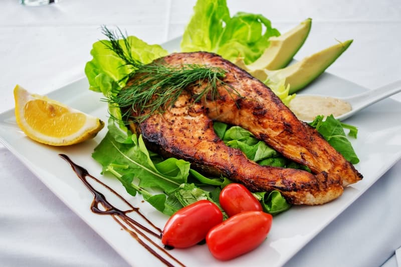 a white plate with fish, tomatoes, avocado and lemon