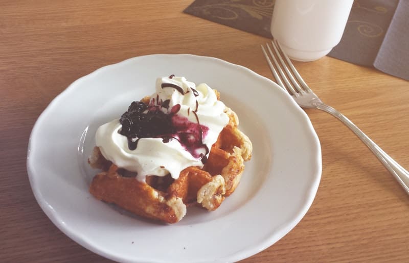 a waffle with whipped cream and blueberry rhubarb sauce on it
