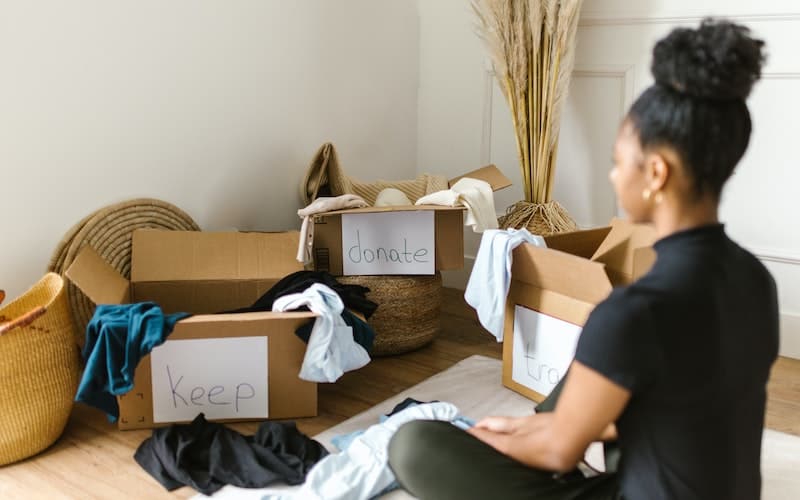 a woman sitting with three boxes and messy clothes pile