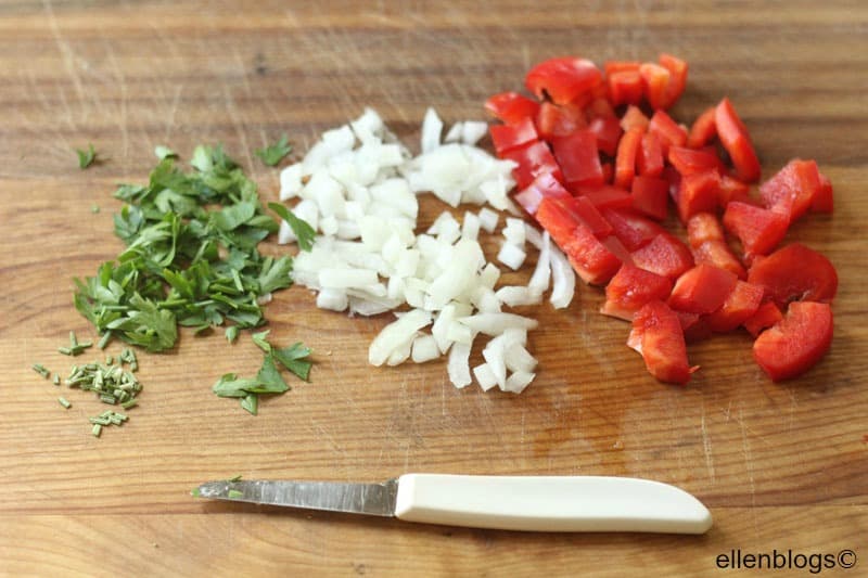 peppers onions and herbs on a cutting board with a white knife
