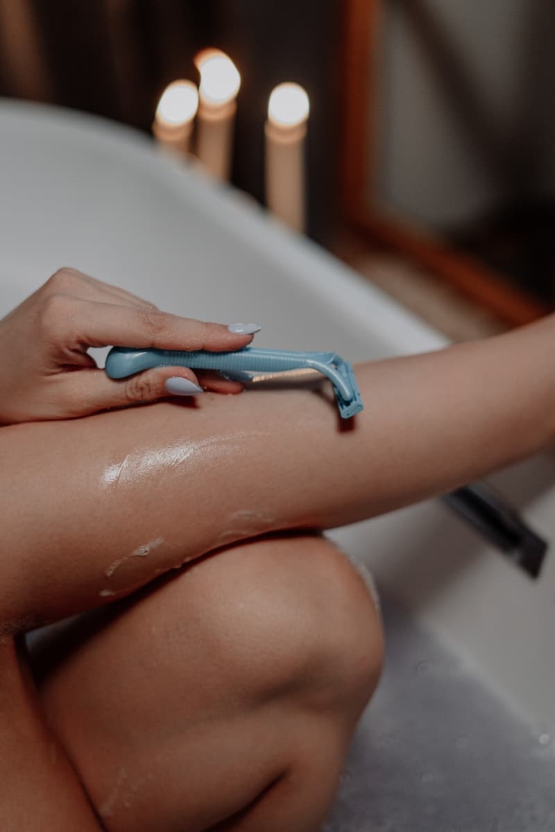 a woman shaving her legs in the tub with a blue razor
