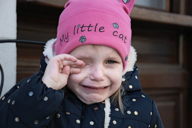 little girl wearing a pink hat crying