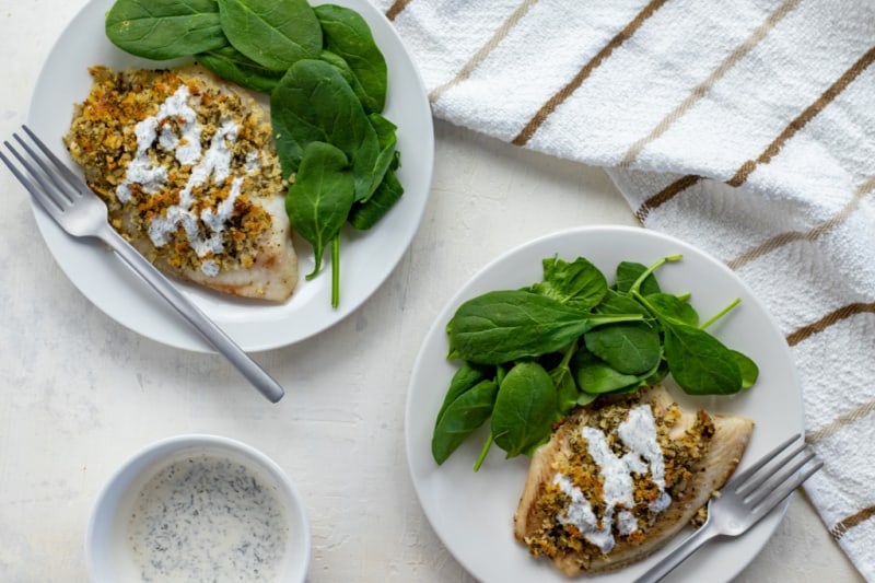 two white plates with white fish on it with baby spinach on the side