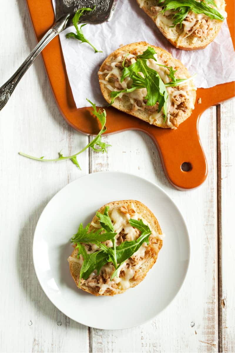 open faced sandwiches on a cutting board topped with arugula