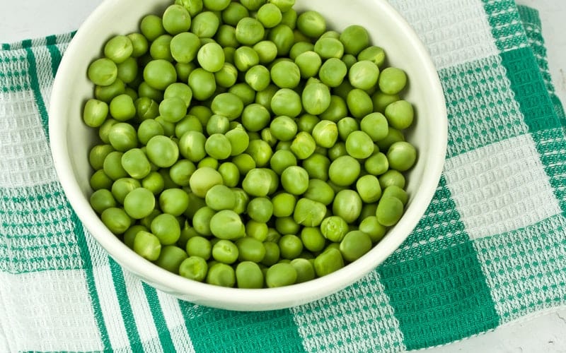 a bowl of peas on a blue and white cloth