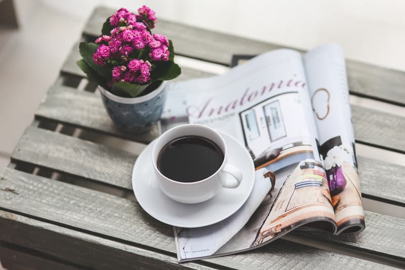 a cup of coffee, a magazine, and a pink plant