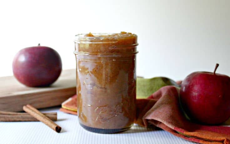 paleo apple butter in a jar with apples and cinnamon sticks