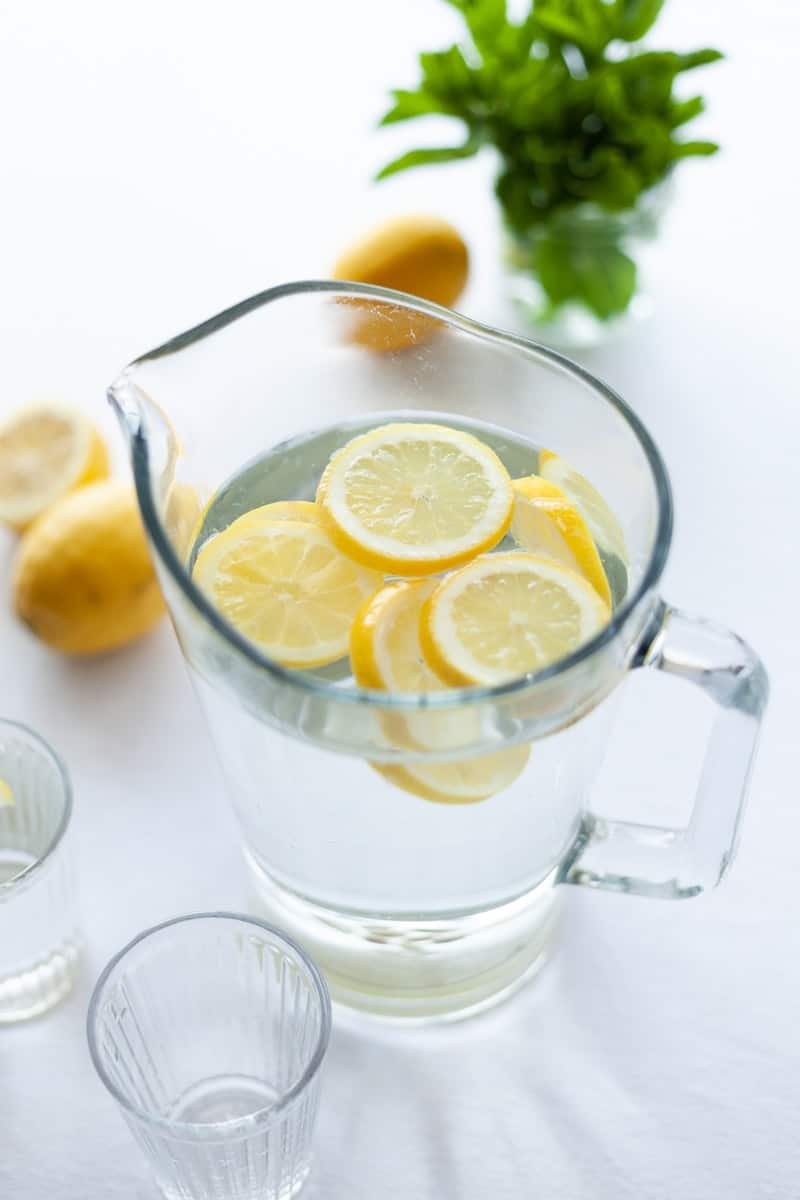 lemon and water in a pitcher with herbs
