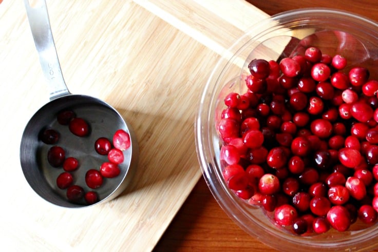 cranberries in a measuring cup and on a wooden cutting board