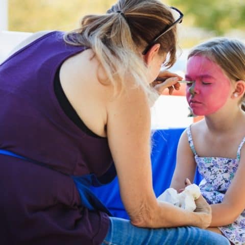 a woman applying face paint on a girl