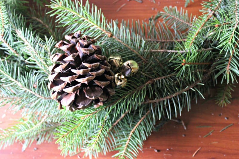 a close up view of an evergreen wreath with a pine cone and jingle bells