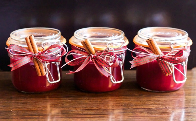 three jars or red jam with cinnamon sticks and bows