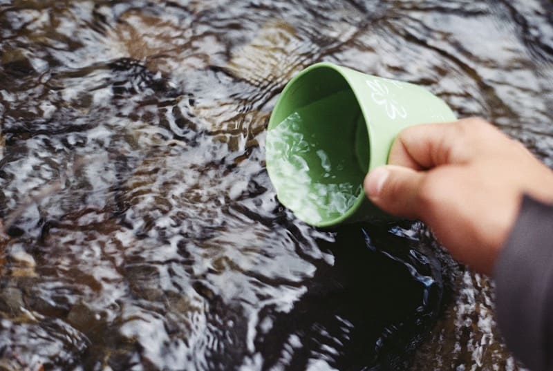 scooping water out of a stream with a green cup