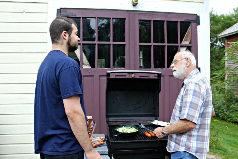 two men standing around the grill cooking dinner