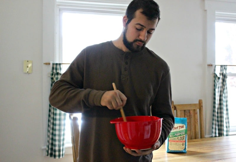 A man holding a red bowl stirring cookie batter