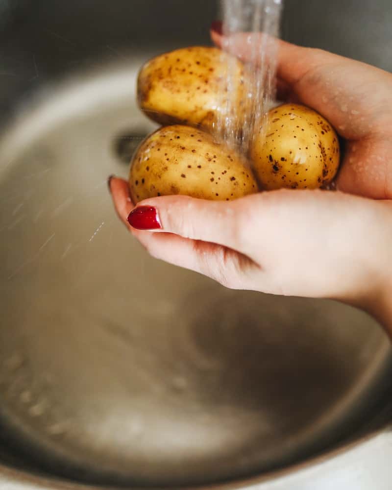 a woman washing potatoes under running water