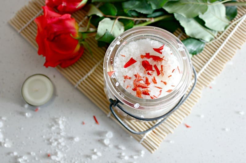 rose scented bath salts with roses and a candle on a white counter