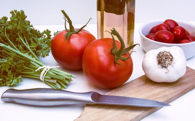 tomatoes garlic and parsley on a cutting board with a silver knife