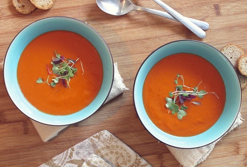 two bowls of tomato soup on a wooden table