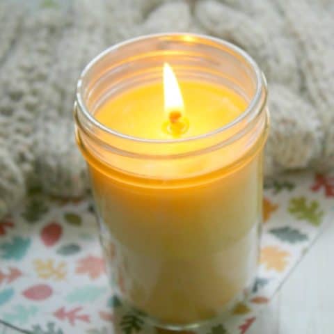 a Mason jar candle burning near a blanket