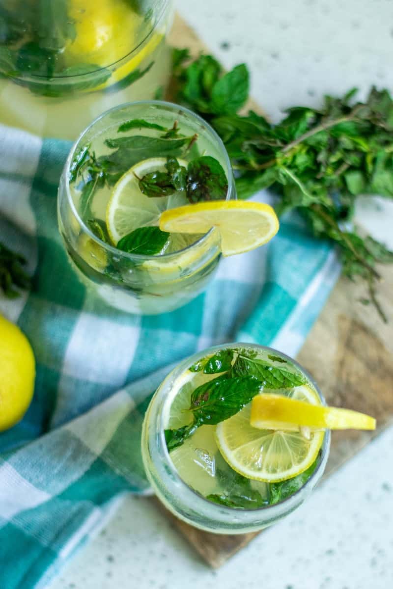 glasses with lemon mint iced tea on a blue cloth and wooden cutting board