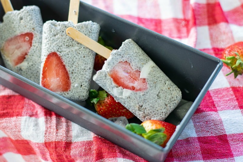 strawberry coconut popsicles on ice in a metal pan