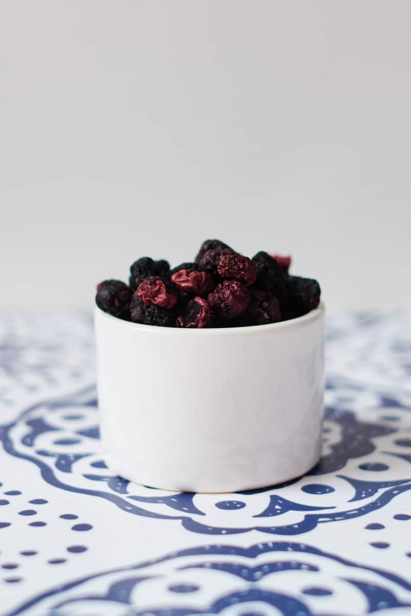 a white cup of dried blueberries on a blue and white surface