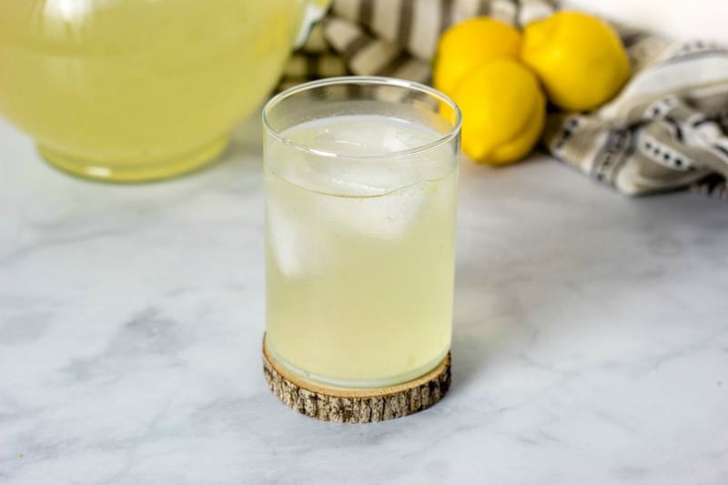 a glass of elderflower lemonade near lemons and a pitcher
