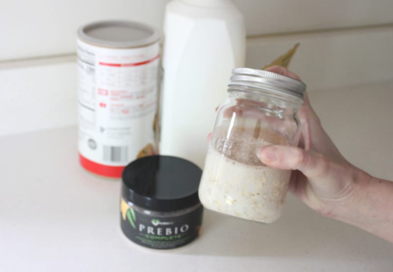 a woman holding a jar of overnight oats with prebiotic powder
