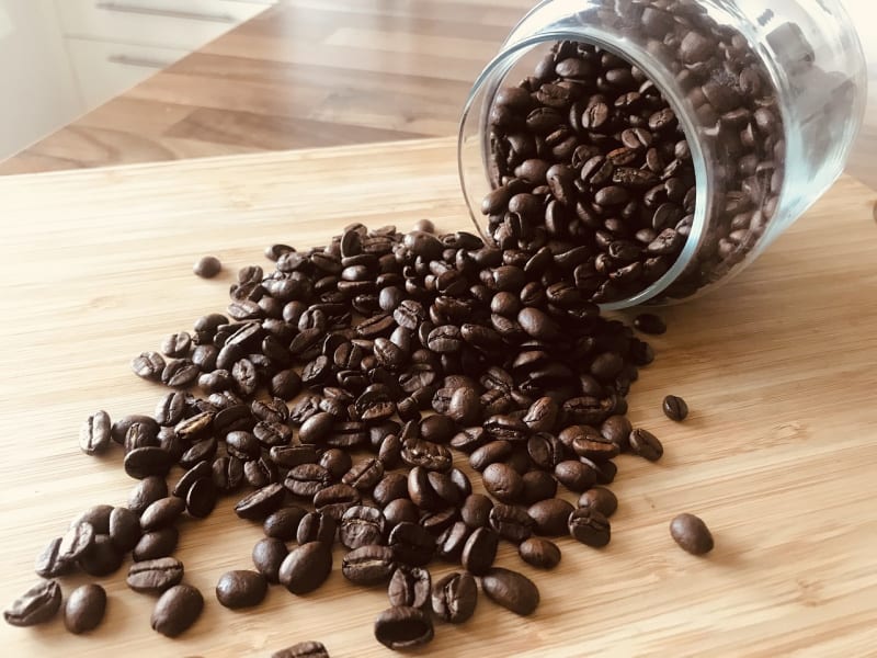coffee beans spilling out of a clear jar on a wooden surface