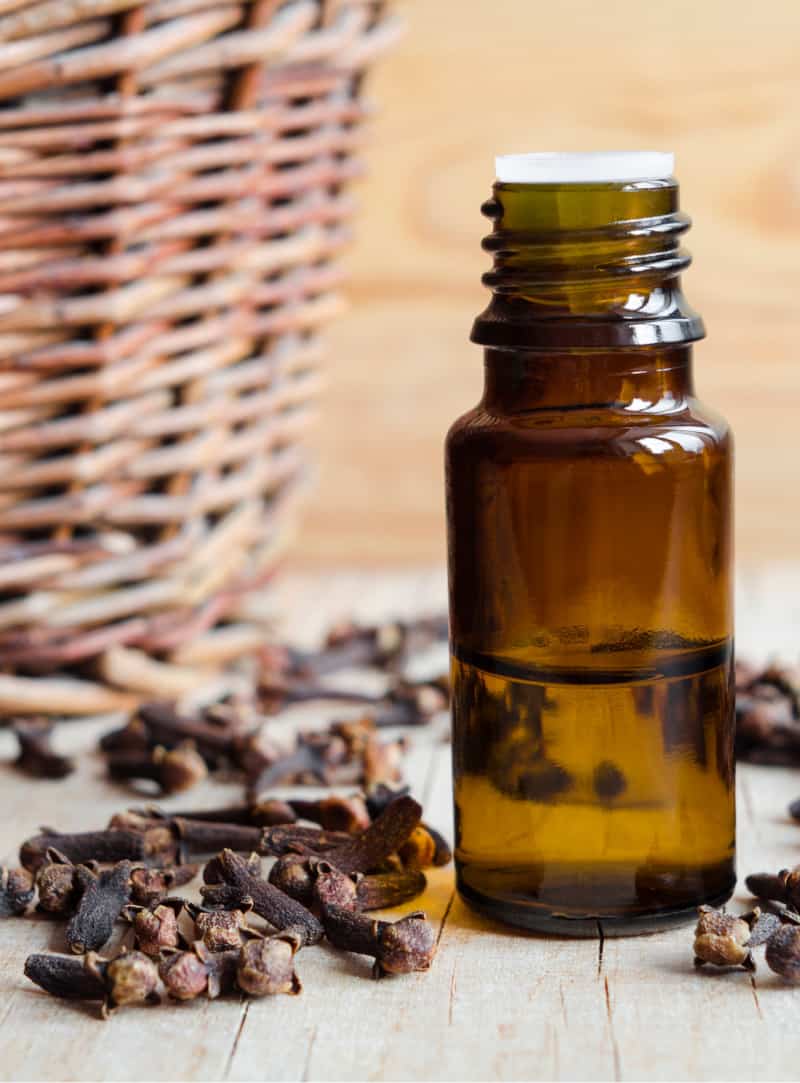 a bottle of clove essential oil in front of a basket
