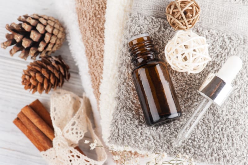 a brown bottle on wash cloths with pine cones and cinnamon