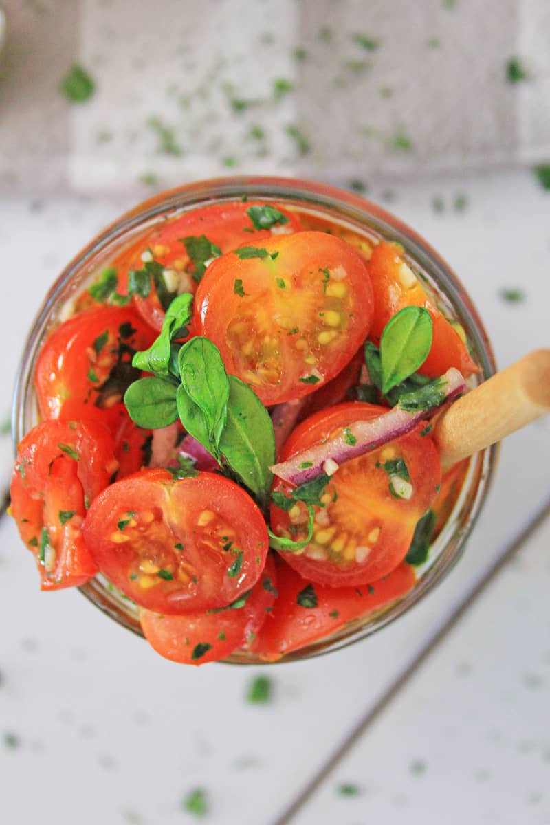 a jar with brightly colored tomatoes and herbs with a wooden spoon