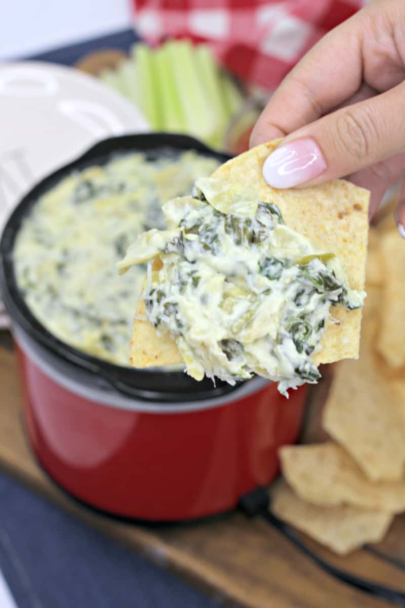 a woman dipping tortilla chips into a spinach dip