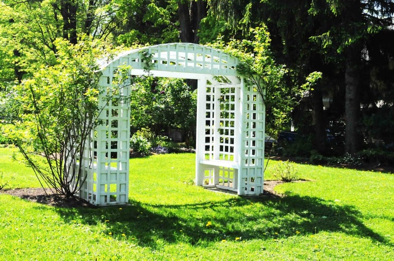 a white trellis in a back yard with green grass