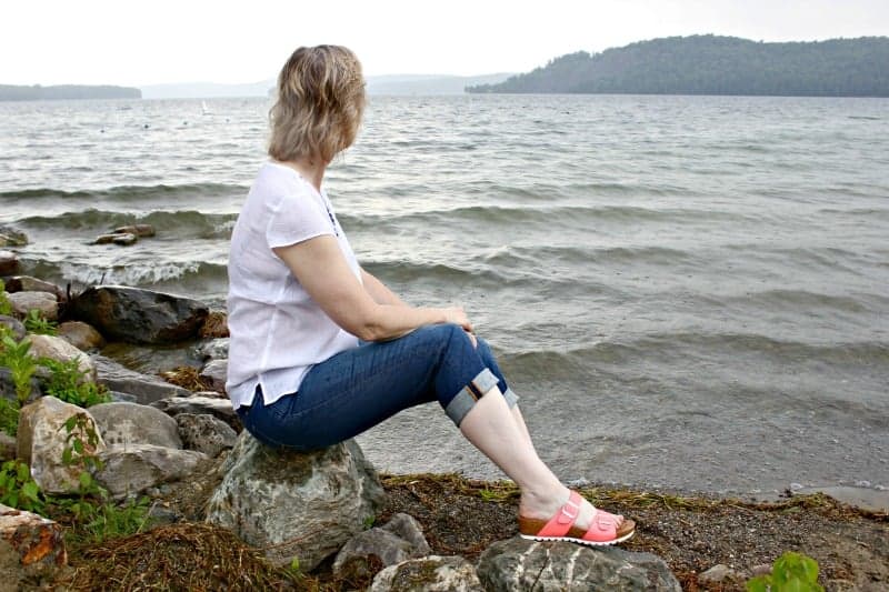 a woman sitting on a rock looking over the lake
