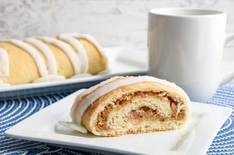a slice of nut roll on a white plate with a white coffee cup