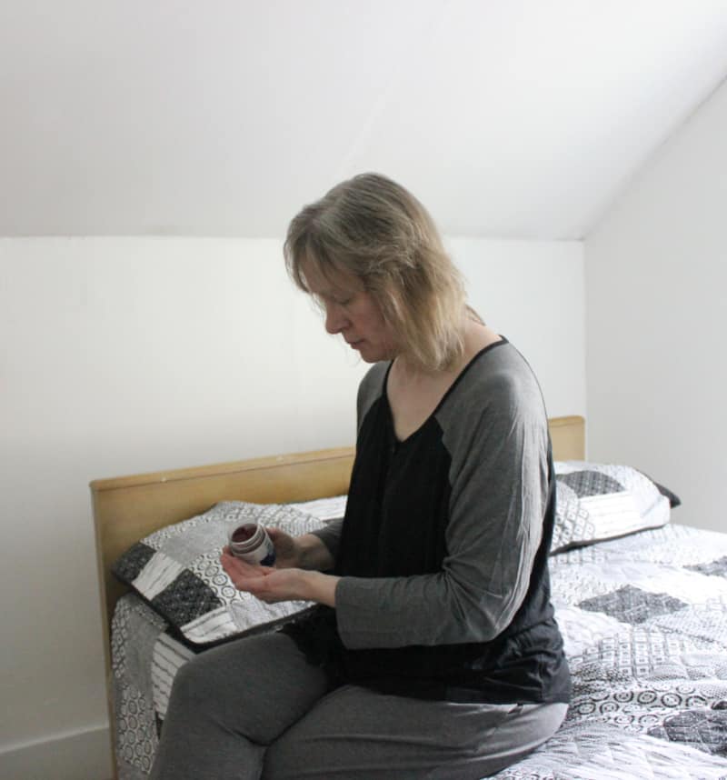 woman wearing grey pajamas sitting on the bed holding a supplement