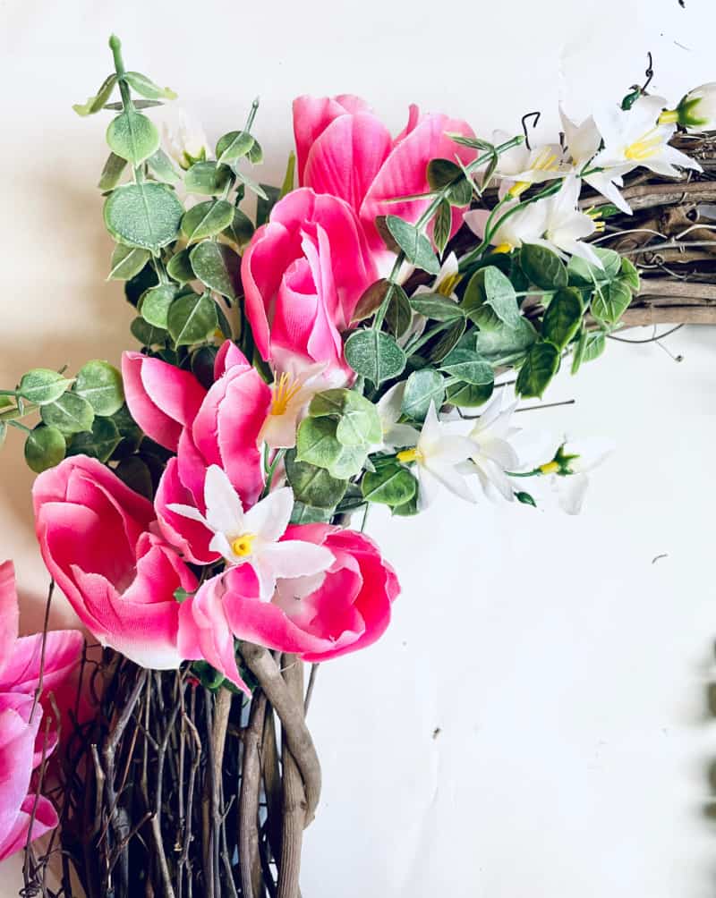 adding pink flowers and greenery to a grapevine form