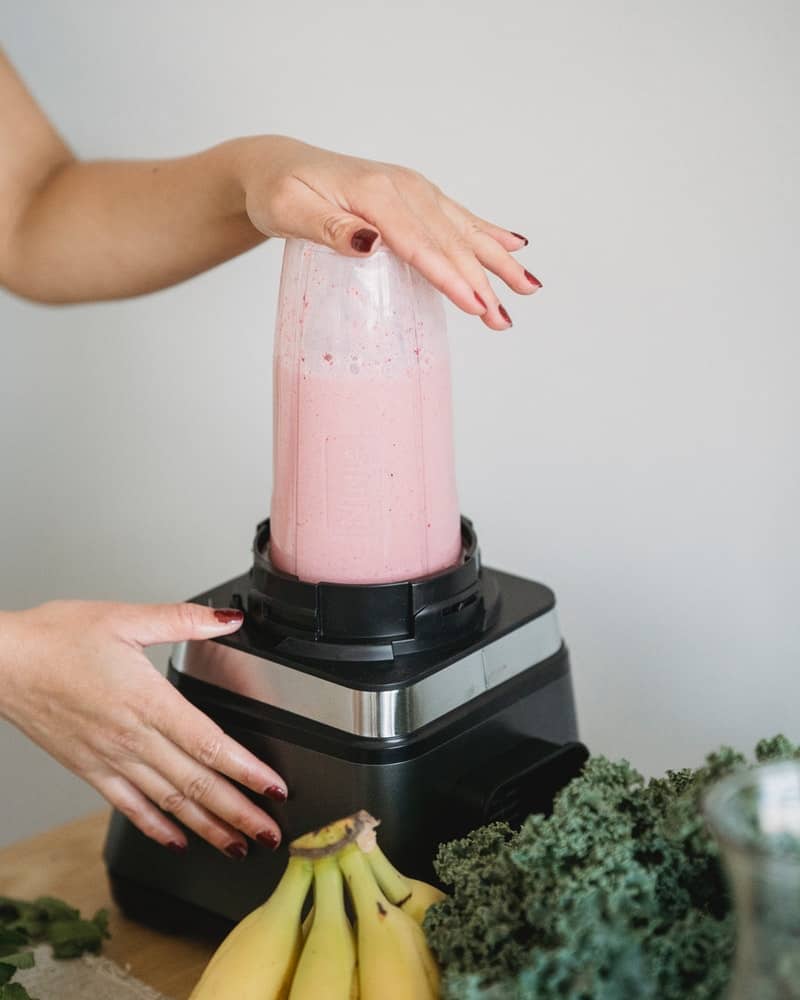 a woman making a pink smoothie in a blender
