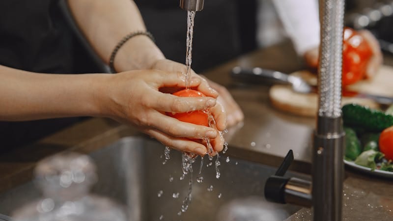 woman washing vegetable under kitchen faucet with running water